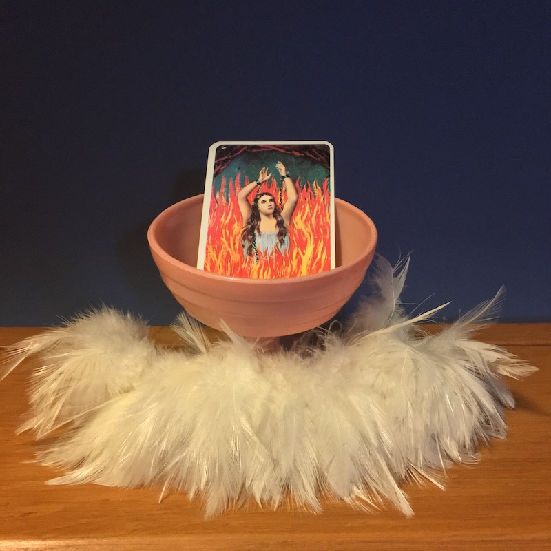 photo of a pink ice cream dish surrounded by white feathers with an image of a woman in flames in the dish
